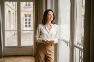 Femme en chemisier en soie ivoire oversize et pantalon camel dans un appartement parisien, style éditorial mode 2026