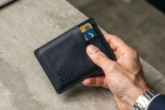 Portefeuille homme personnalisé en cuir marine avec monogramme gravé tenu à la main sur bureau en béton