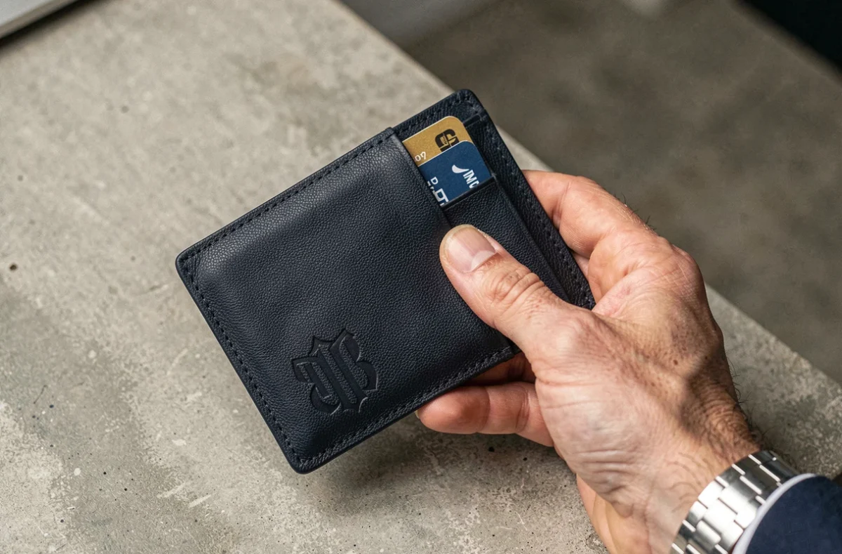 Portefeuille homme personnalisé en cuir marine avec monogramme gravé tenu à la main sur bureau en béton
